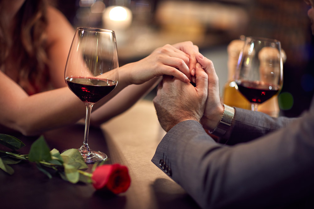 Couple holding hands over dinner with wine and red rose