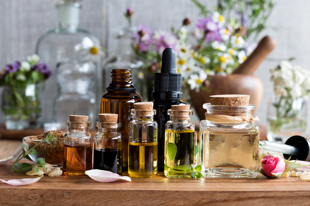 Bottles of essential oils with plants and herbs in background