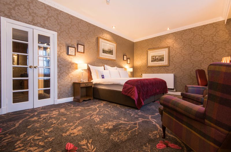 Generous living space with a bed and armchairs in large hotel rooms at Kingsmills Hotel, Inverness