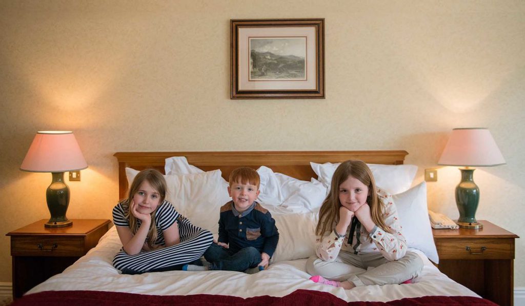 Three children sitting on a bed in a luxury family room at Kingsmills Hotel