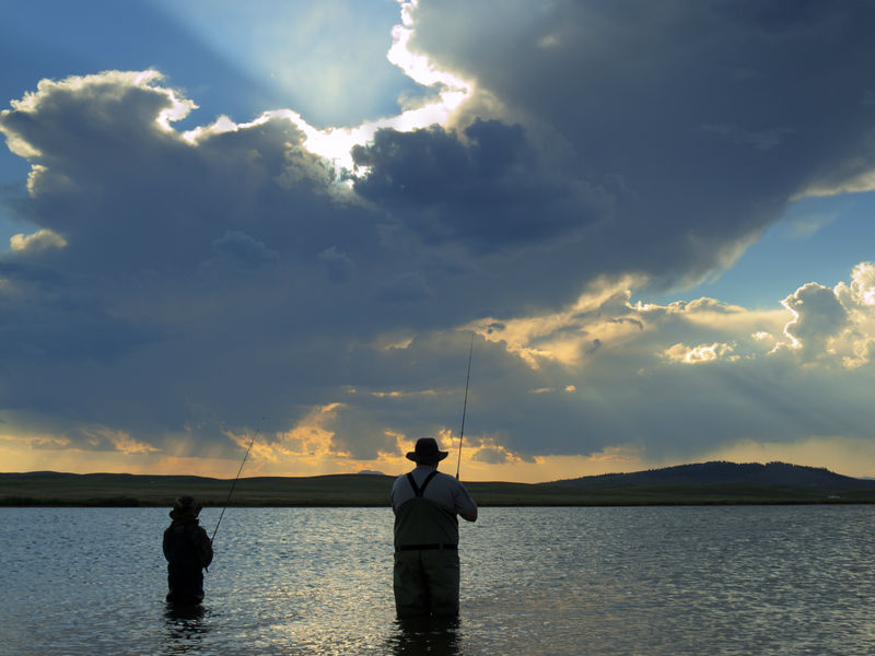 A man and boy fishing a loch at dusk.