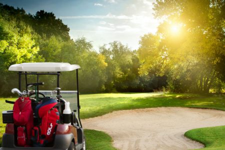 A golf cart by a sand pit with a setting sun.