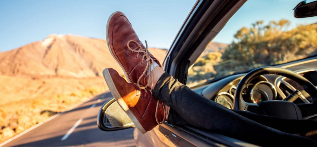 A person sitting in a car with their feet out a window