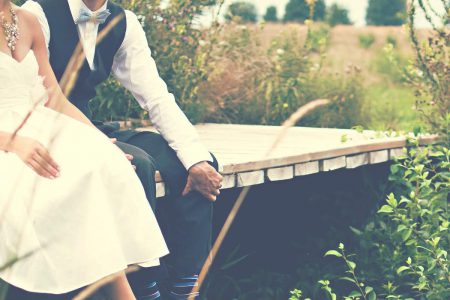 A bride and groom sitting on a small bridge over a little stream in theri wedding outfits.