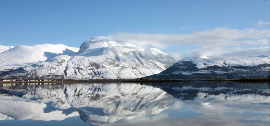 Snowy mountains in the Highlands reflecting in a still Loch