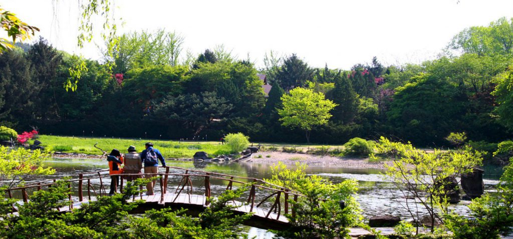 Three people sitting on a small wooden bridge striding a river.