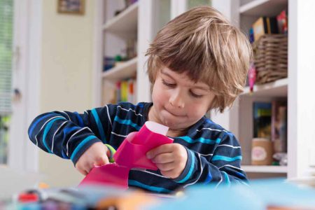 A young boy cutting up some craft paper