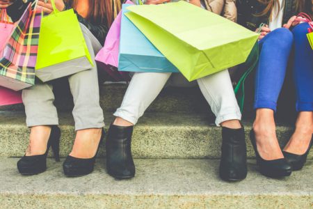 A close up of the legs and colourful shopping bags of ladies sat on some steps.