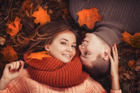 Couple lying head to head on the ground with autumn leaves around them