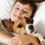 a boy cuddling his dog in bed