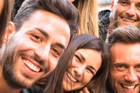 A reunion of a group of friends gathered around a camera and taking a selfie