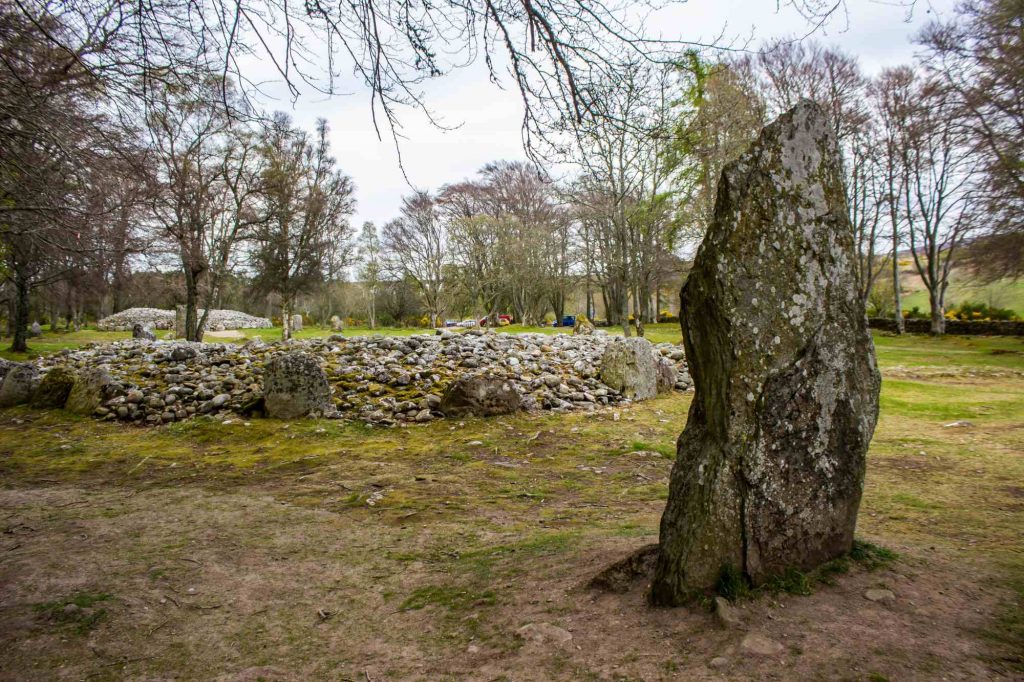 An image of the Clava Cairns sheltered in a grove of beech trees alongside a large standing stone.