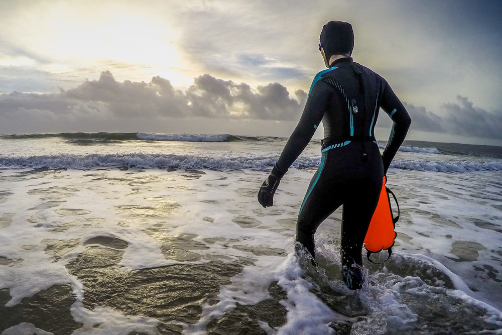 Wild swimmer entering the water in a wetsuit with a tow float