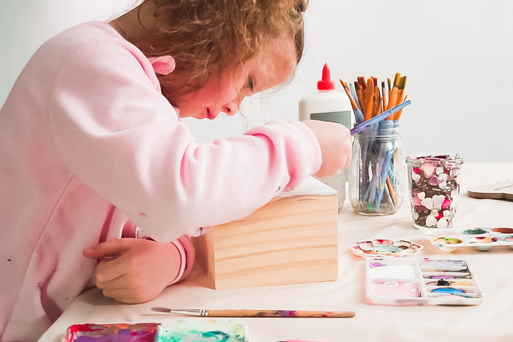 Child decorating a wooden box with paints