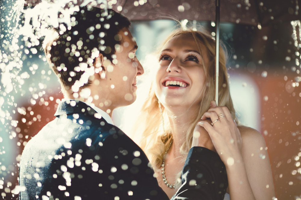 Bride and groom standing in the rain under an umbrella