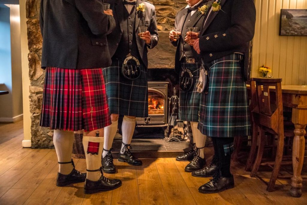 4 men stood around a fire in Scottish Kilts with a dram