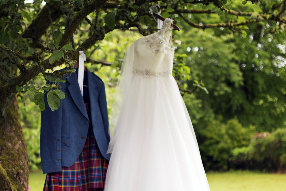 A wedding dress and kilt suit hanging in a tree