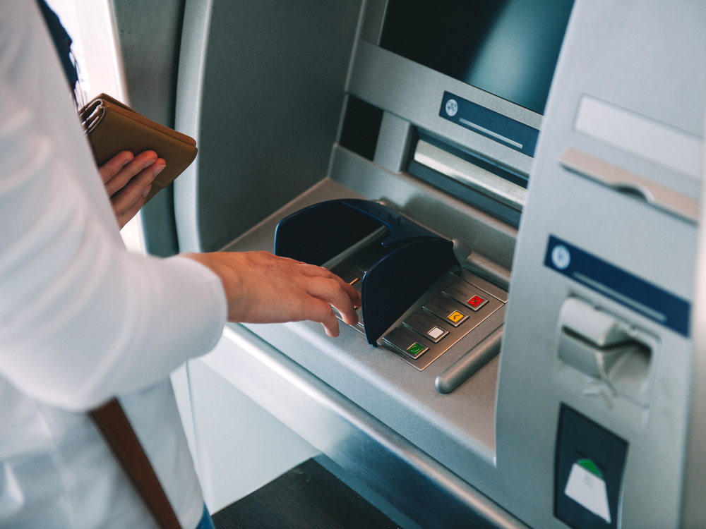 Woman using ATM holding wallet an pressing the PIN security number on the keyboard automatic teller machine.