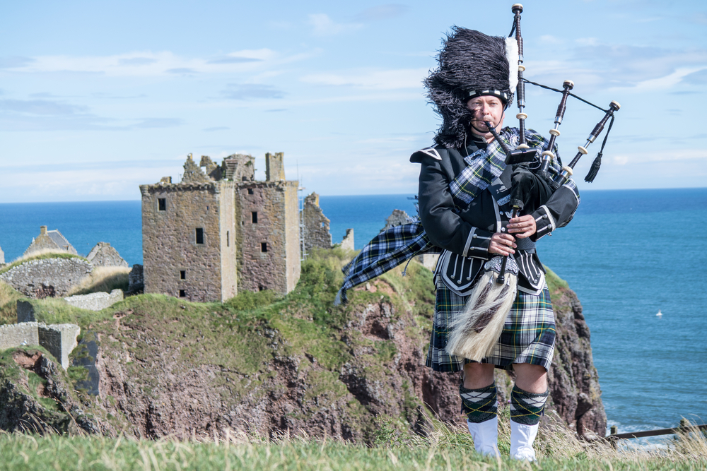 Traditional scottish bagpiper in full dress code at Dunnottar Castle in Stonehaven