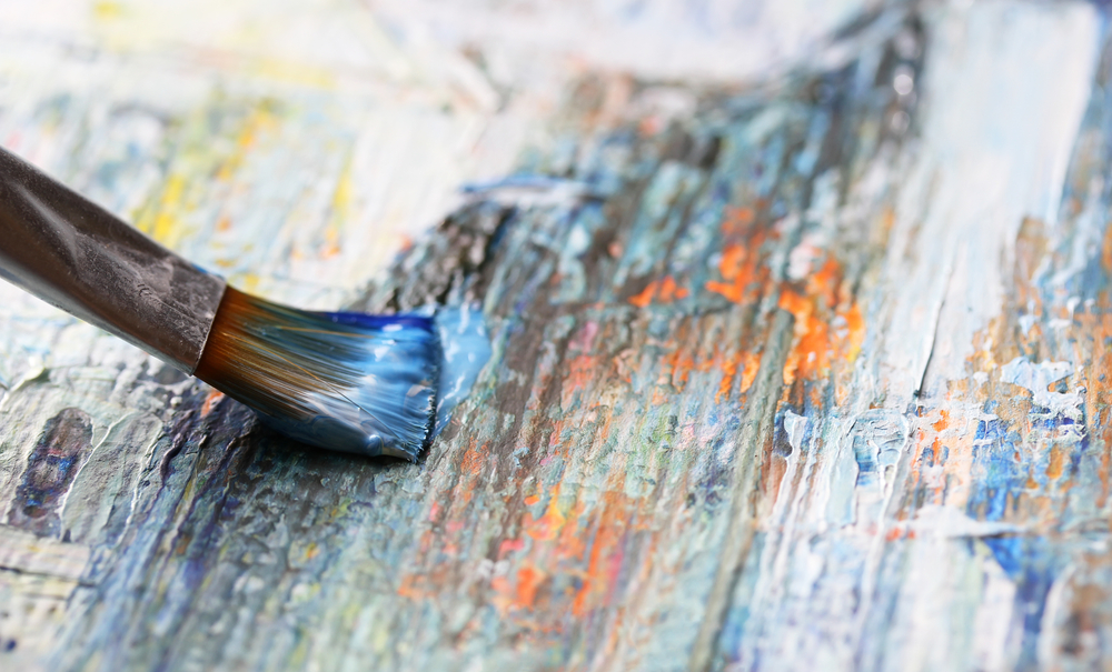 Closeup of brush with paint on painting a canvas of abstract art.