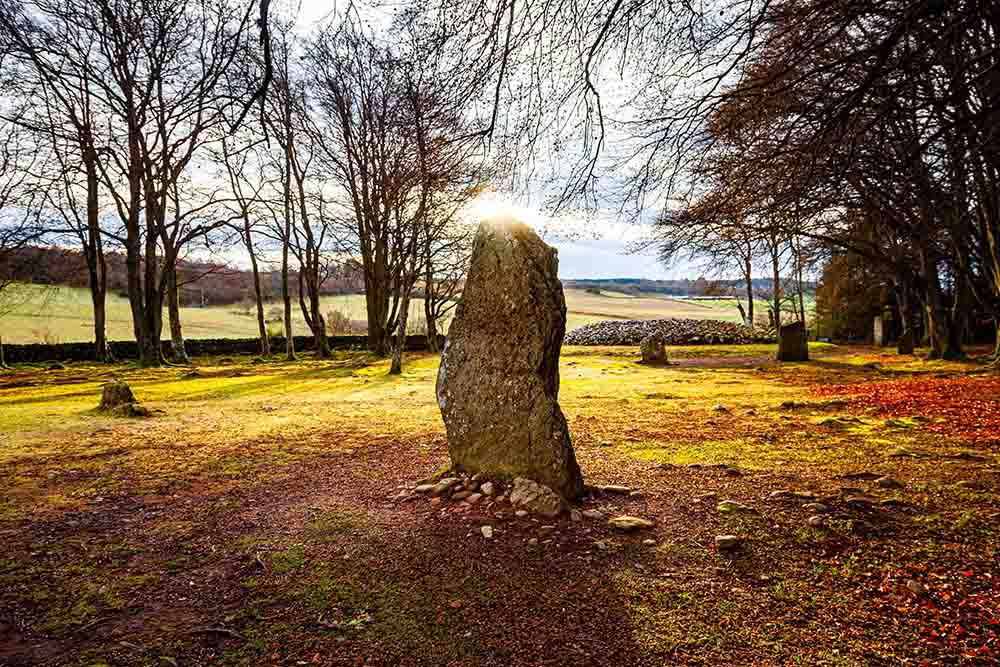 A standing stone with the sun glowing behind it at Clava Cairns.