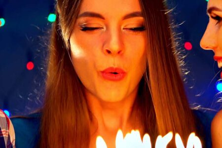 A lady, surrounded by friends, blows out candles on her birthday cake.