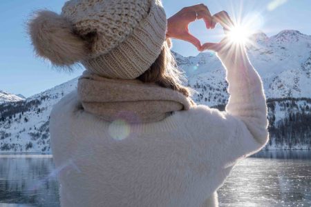A lady stands on the banks of Loch Ness on a beautiful winters day making a love heart frame with her hands.