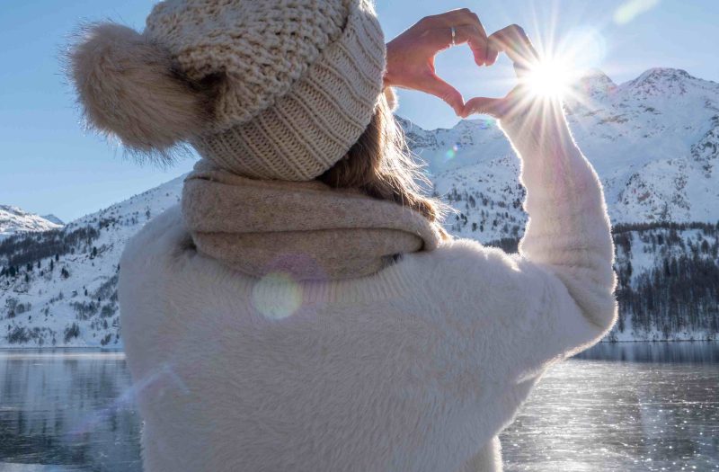 A lady stands on the banks of Loch Ness on a beautiful winters day making a love heart frame with her hands.